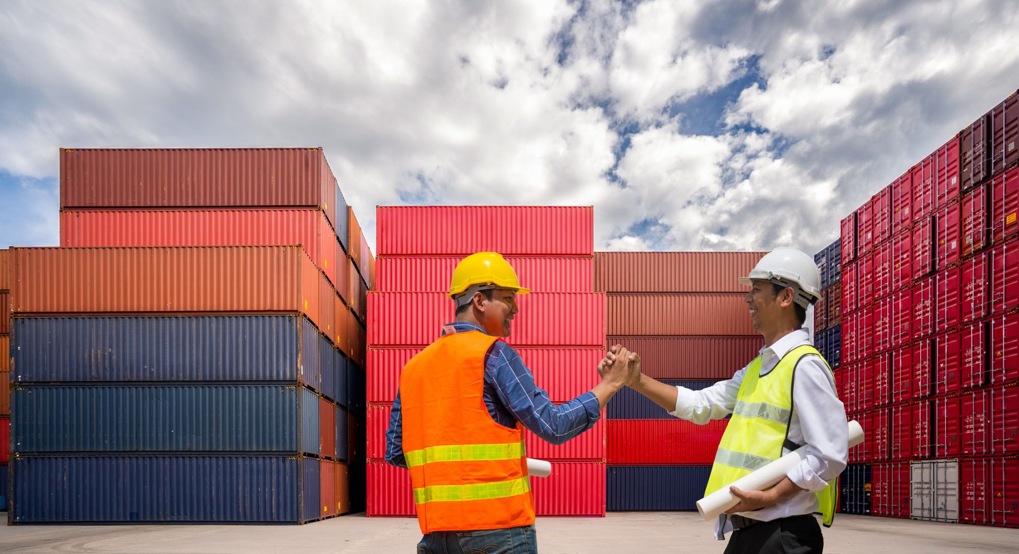 Logistics professionals shaking hands in front of shipping containers